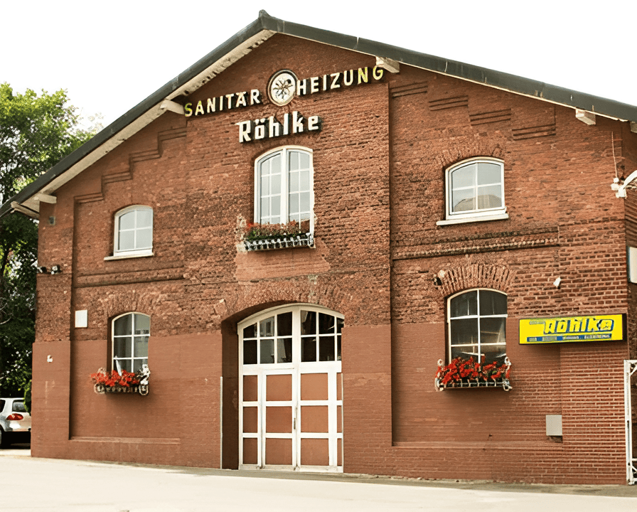 Das Firmengebäude der Hans-Georg Röhlke GmbH in Lüneburg, ein Backsteinhaus mit der Aufschrift "Sanitär - Heizung Röhlke" und Blumenkästen an den Fenstern.